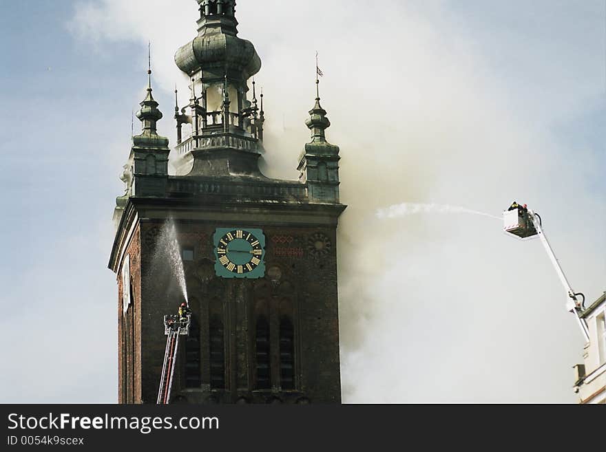 Two fire engine appliances spraying water on burning clock tower building. Two fire engine appliances spraying water on burning clock tower building.