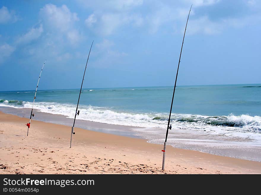 Three fishing poles sit at the beach waiting for a catch. Three fishing poles sit at the beach waiting for a catch