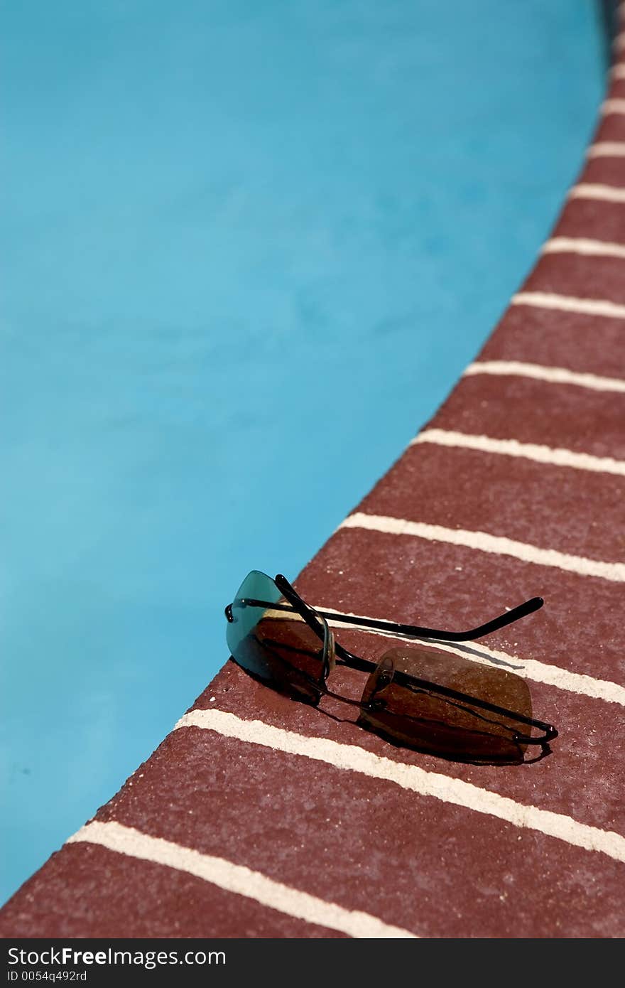 A pair of sun glasses by a pool. A pair of sun glasses by a pool