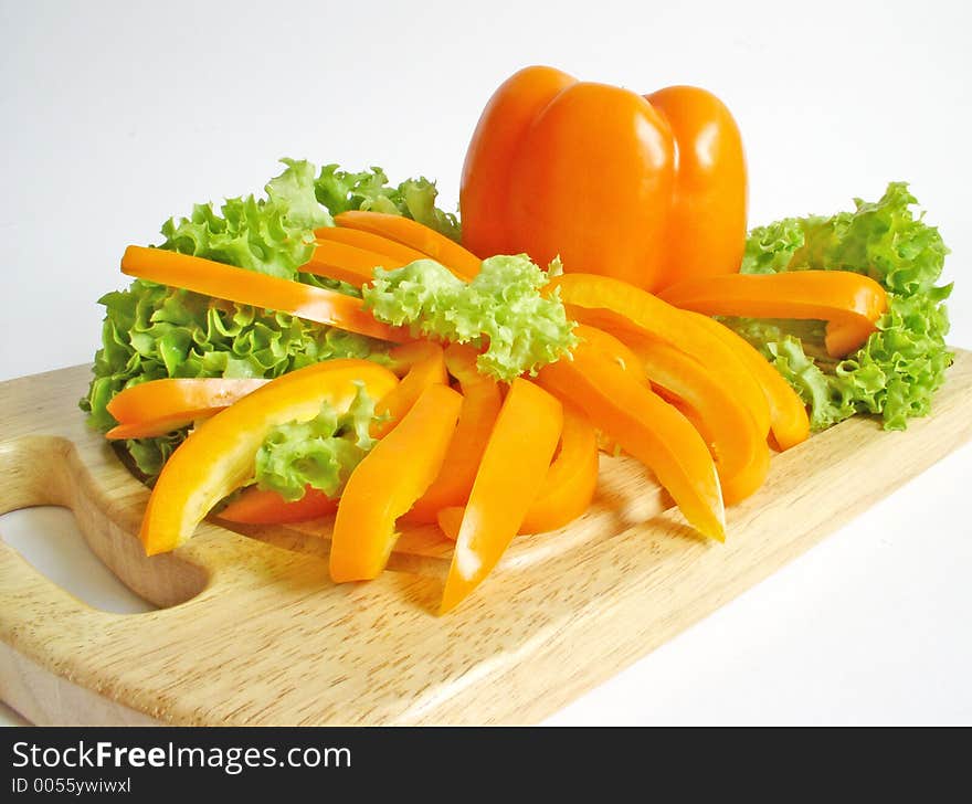 Orange paprika and lettuce on breadboard isolated