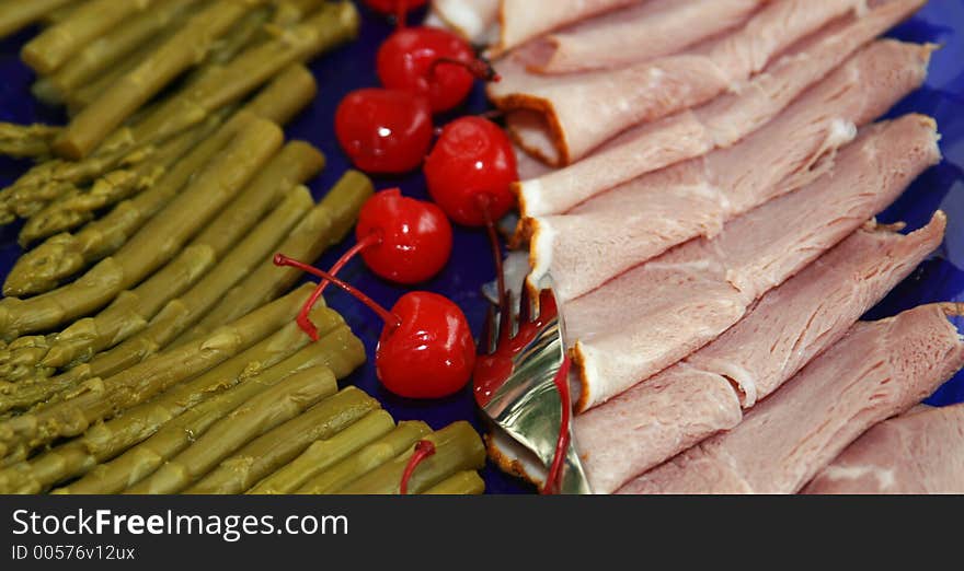 Asparagus, cherries and sliced ham on a deep blue plate, ready to be served at a party. Asparagus, cherries and sliced ham on a deep blue plate, ready to be served at a party