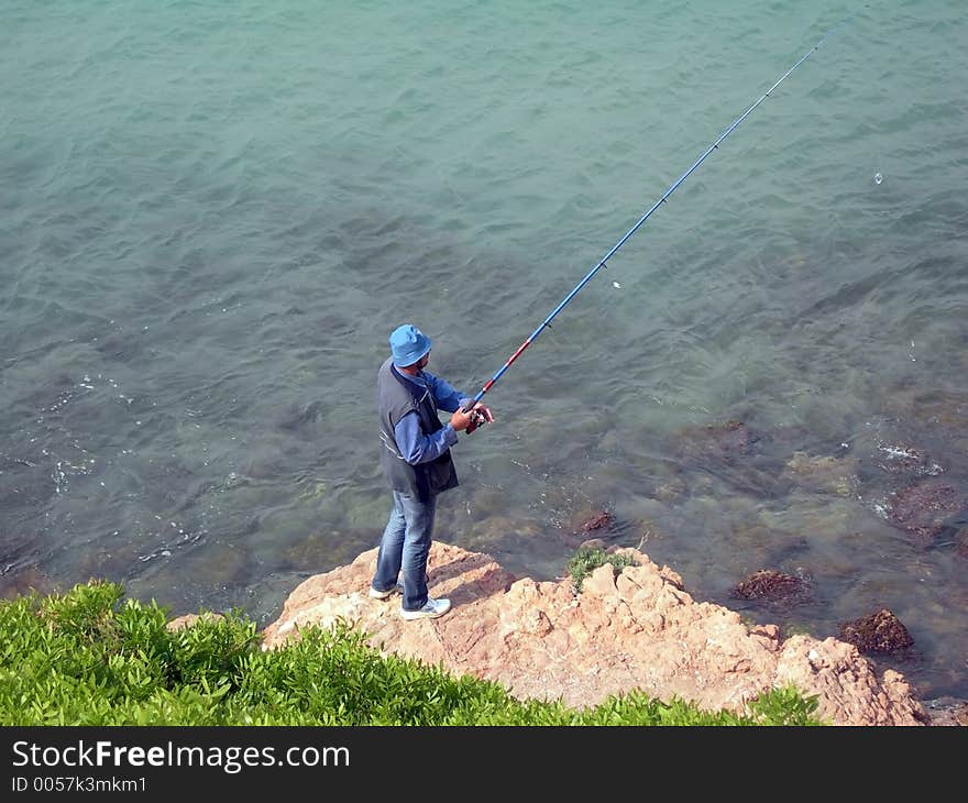 Man in blue fishing on a rock. Man in blue fishing on a rock