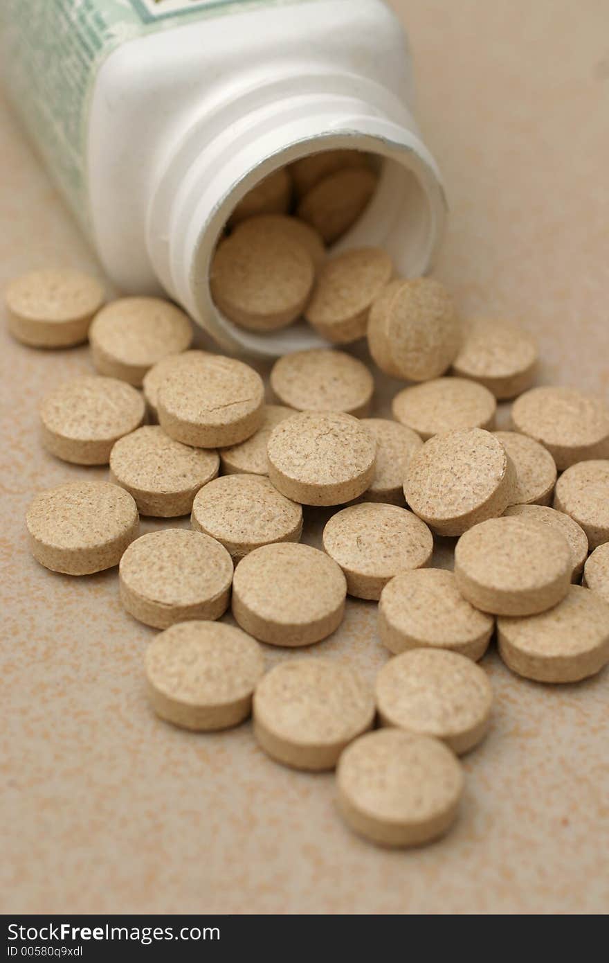 Bottle opening with brown circular pills spilled out onto table surface