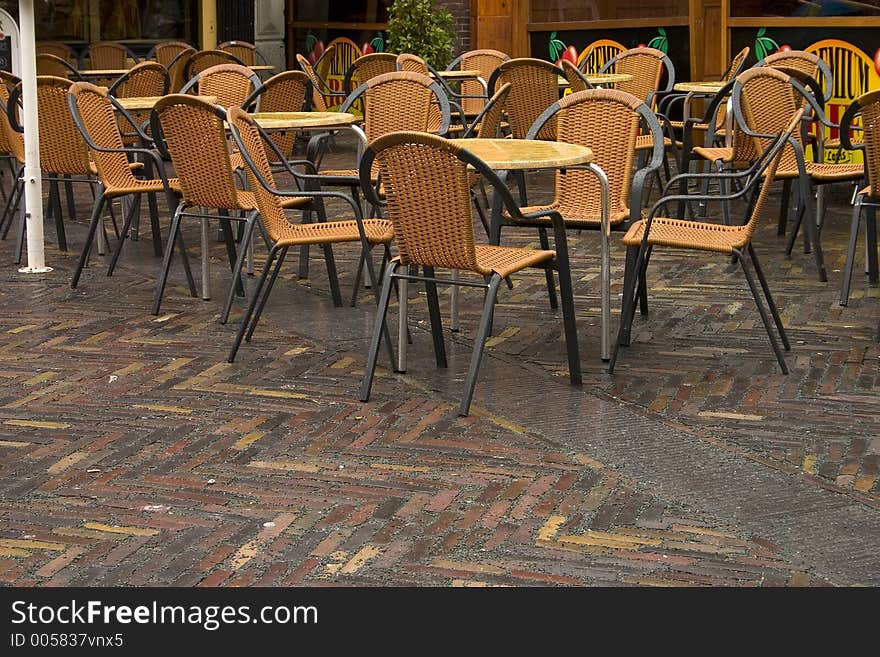 A group of wet restaurant chairs sit unoccupied. A group of wet restaurant chairs sit unoccupied