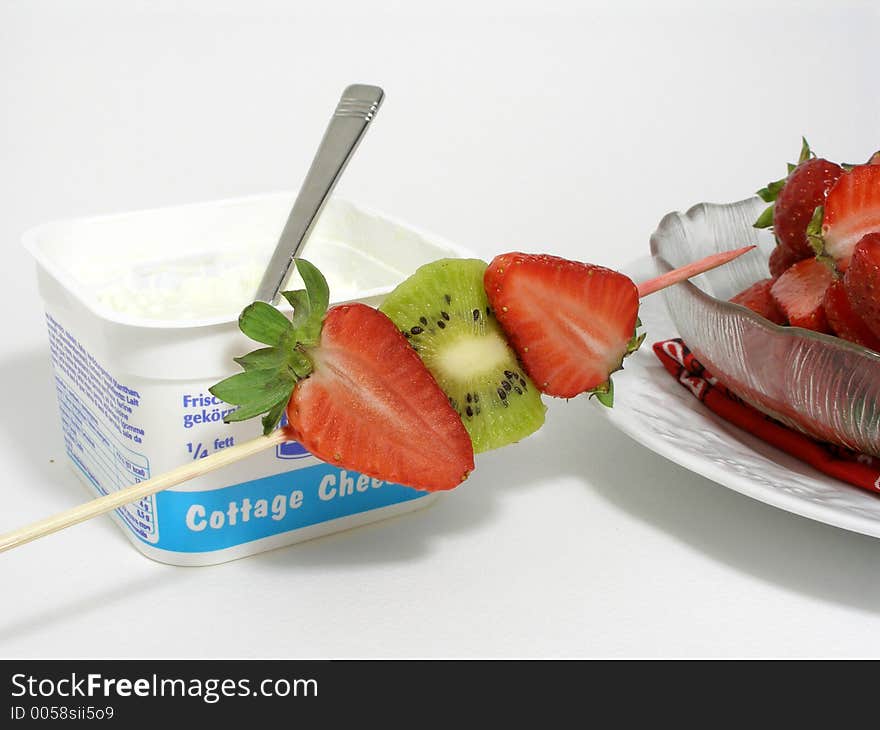 Cottage cheese in its plastic container with a fruits skewer and a bowl of strawberries. Cottage cheese in its plastic container with a fruits skewer and a bowl of strawberries