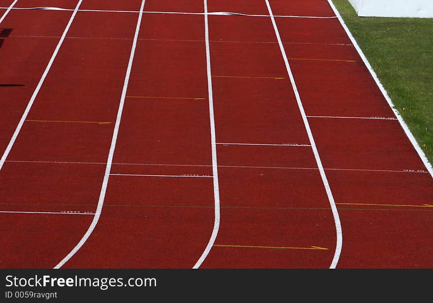 Straight red running track with white dividing lines part of grass visible. Straight red running track with white dividing lines part of grass visible