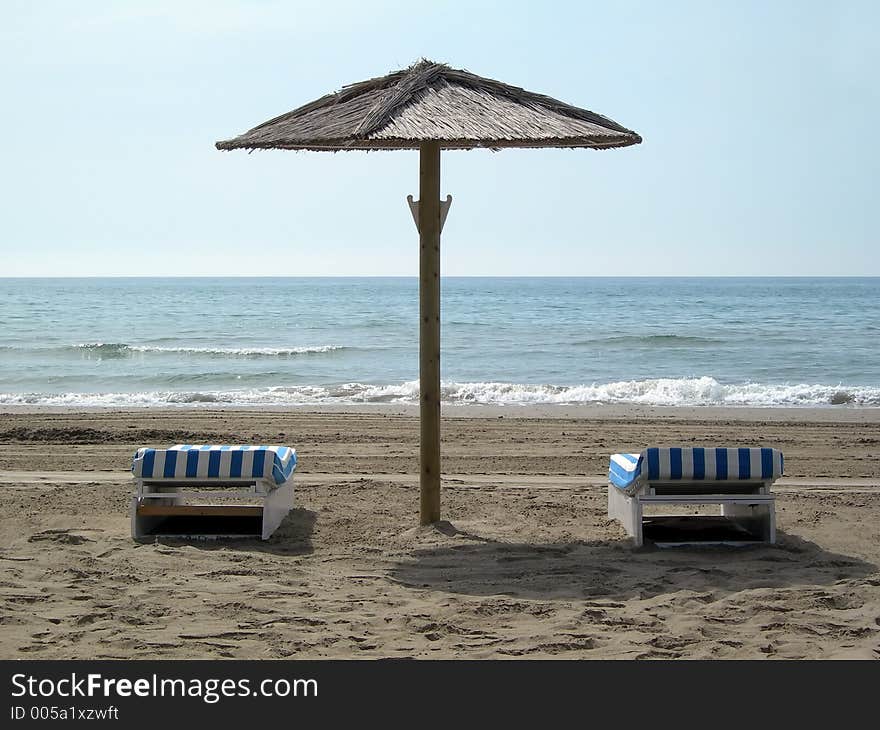 Two chairs under an umbrella in the beach. Two chairs under an umbrella in the beach