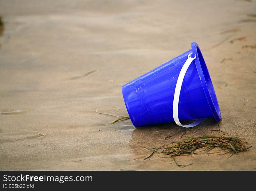 Close up image of a wet sand blue bucket alone in the tropical sand. Close up image of a wet sand blue bucket alone in the tropical sand