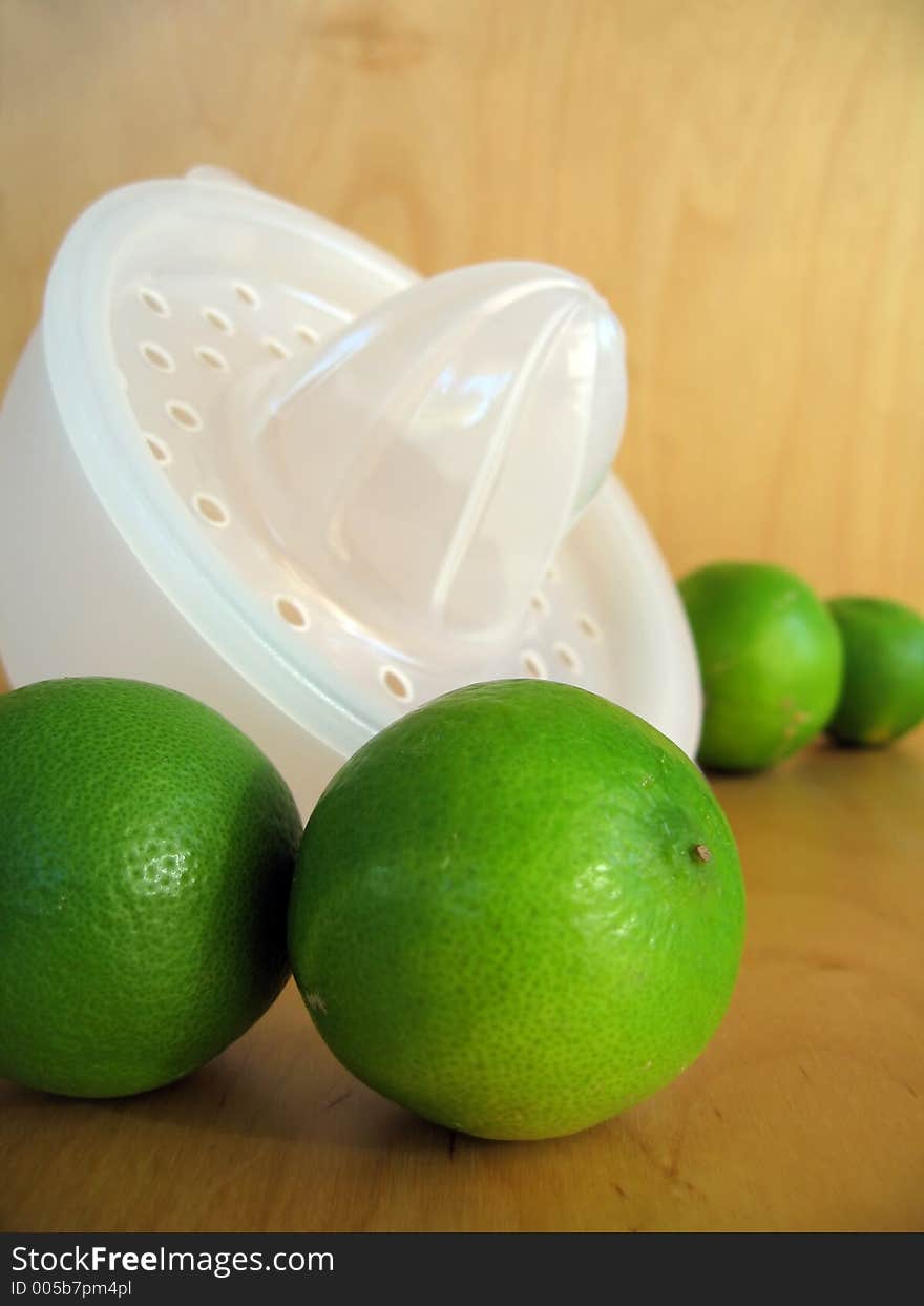 A fruit squeezer with fresh green limes. Focused at the limes in the foreground. A fruit squeezer with fresh green limes. Focused at the limes in the foreground.