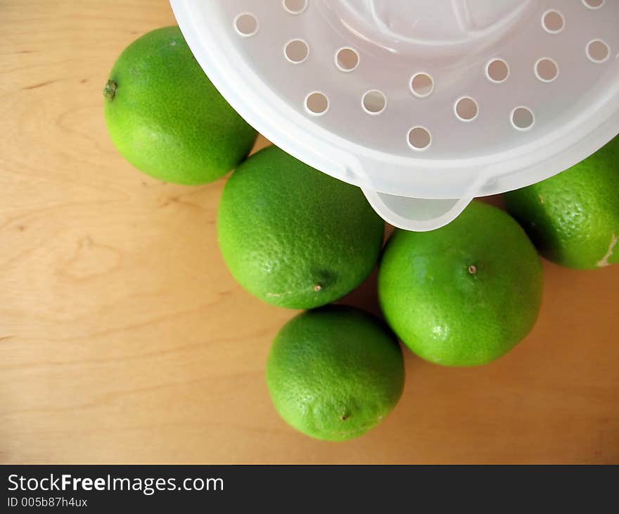 A fruit squeezer with fresh green limes. Focused at the fruit squeezer. A fruit squeezer with fresh green limes. Focused at the fruit squeezer.