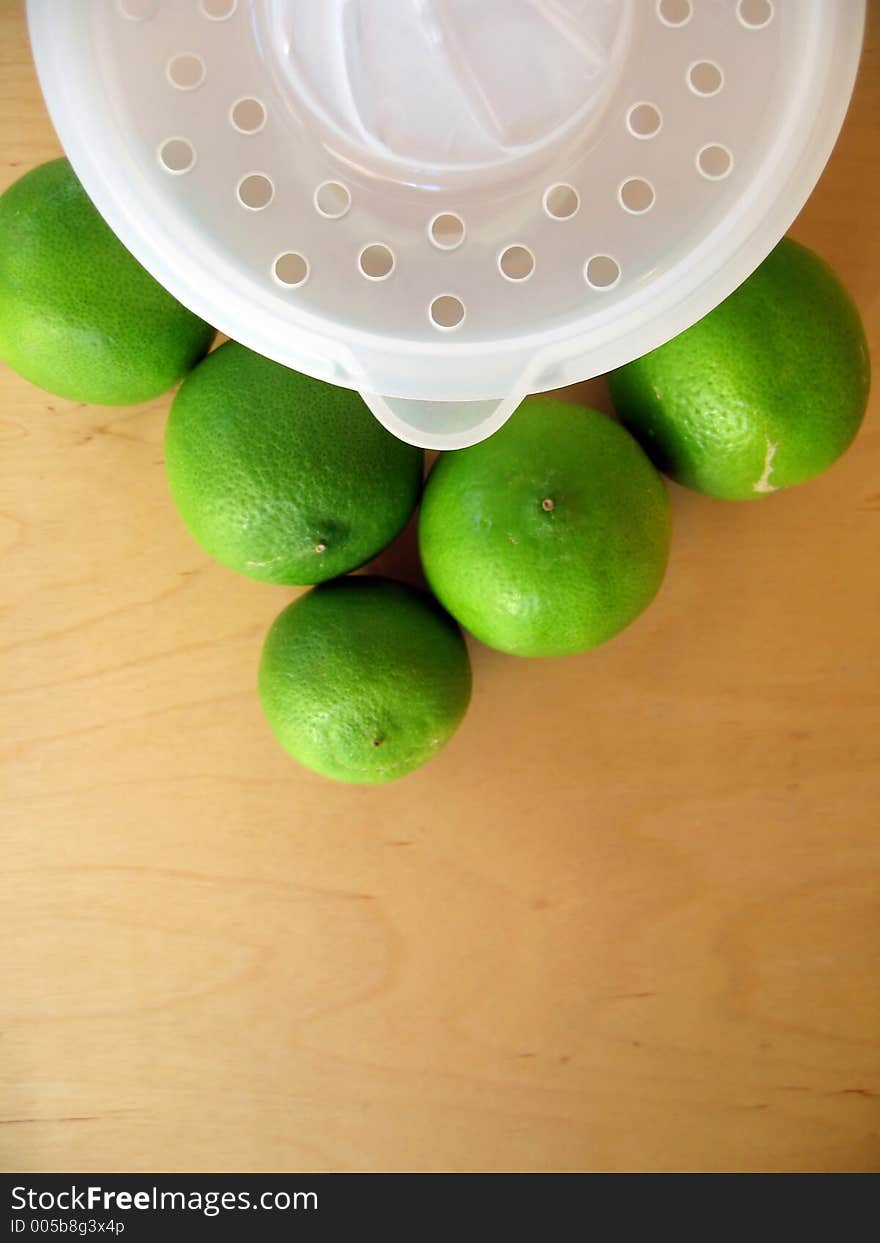 A fruit squeezer with fresh green limes. Focused at the fruit squeezer. A fruit squeezer with fresh green limes. Focused at the fruit squeezer.