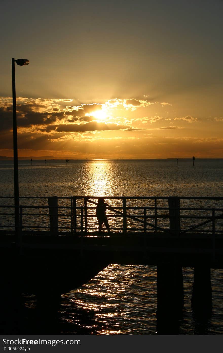 A small child playing in the last rays of light of the day on a jetty. Beautiful ocean view. Location: Stradbroke Island, Queensland, Australia. A small child playing in the last rays of light of the day on a jetty. Beautiful ocean view. Location: Stradbroke Island, Queensland, Australia.