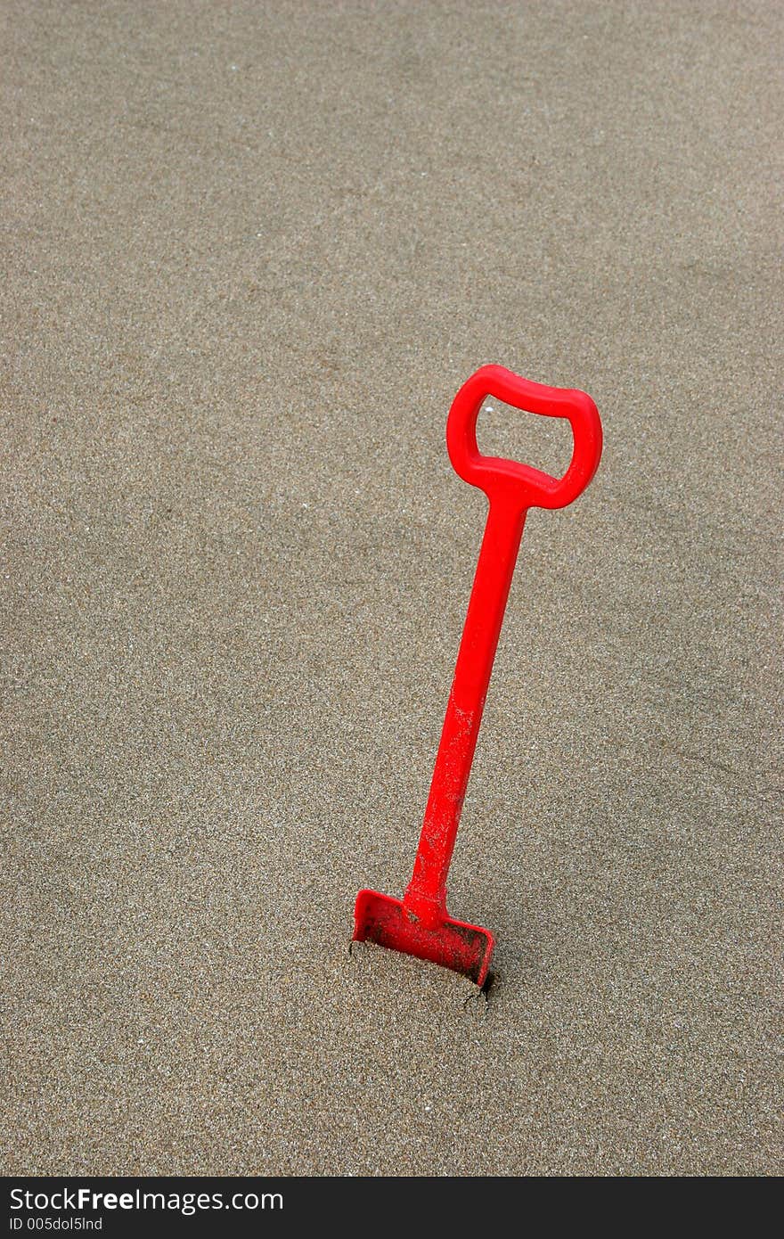 A red shovel on brownish sand with space over to write or add text. A red shovel on brownish sand with space over to write or add text.