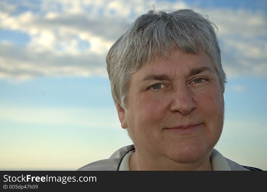 A portrait of a smiling gray-haired woman with the sky as a backdrop. A portrait of a smiling gray-haired woman with the sky as a backdrop.