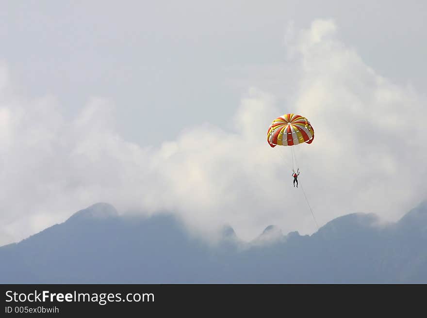 A male vacationer parasailing high in the sky above the mountains of Langkawi Island, Malaysia. The speedboat pulling him is omitted. A male vacationer parasailing high in the sky above the mountains of Langkawi Island, Malaysia. The speedboat pulling him is omitted.