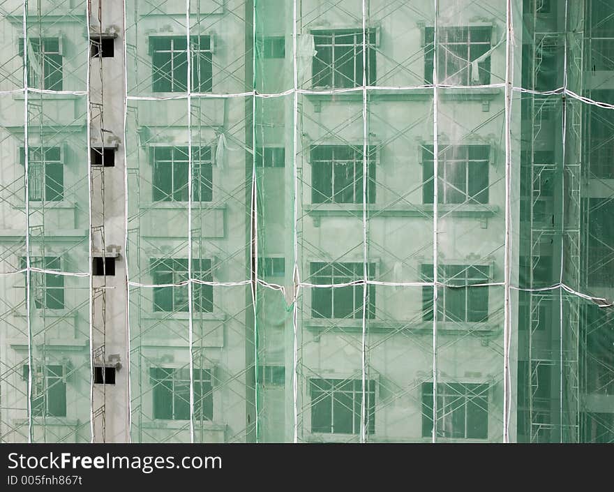 Apartment building under construction with scaffolding and green netting on its exterior. Apartment building under construction with scaffolding and green netting on its exterior.