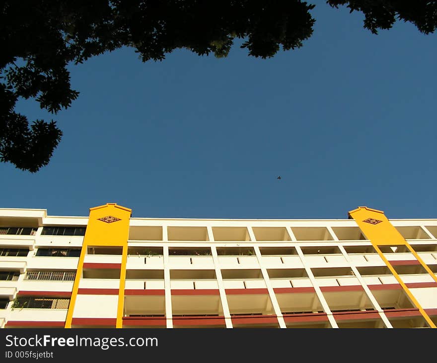 Taken in singapore. location is choa chu kang, taken at sunset which illuminated the side of building. trees are above thus framing the sky. the facade is bright yellow and red with large beige areas. Taken in singapore. location is choa chu kang, taken at sunset which illuminated the side of building. trees are above thus framing the sky. the facade is bright yellow and red with large beige areas