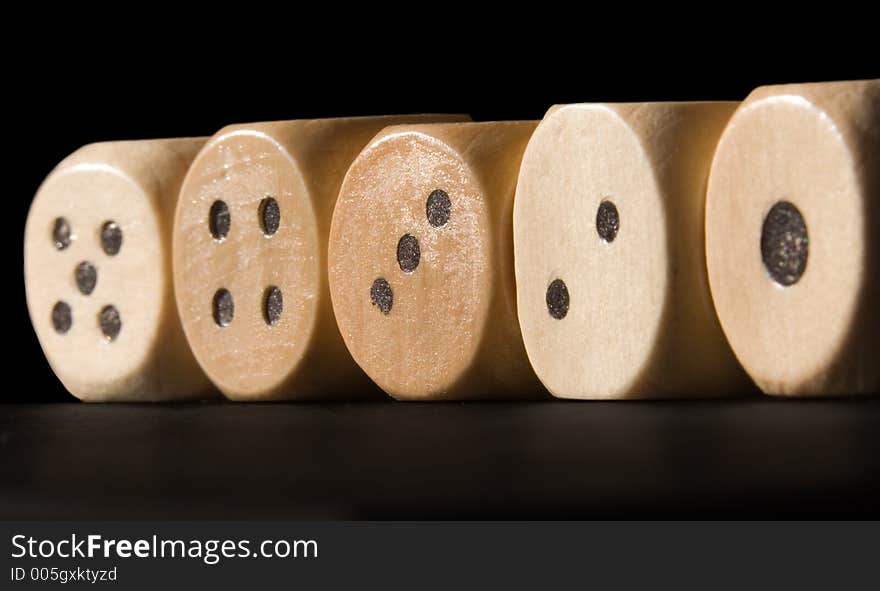 Straight row of wooden dice lit by the sun against a black background.