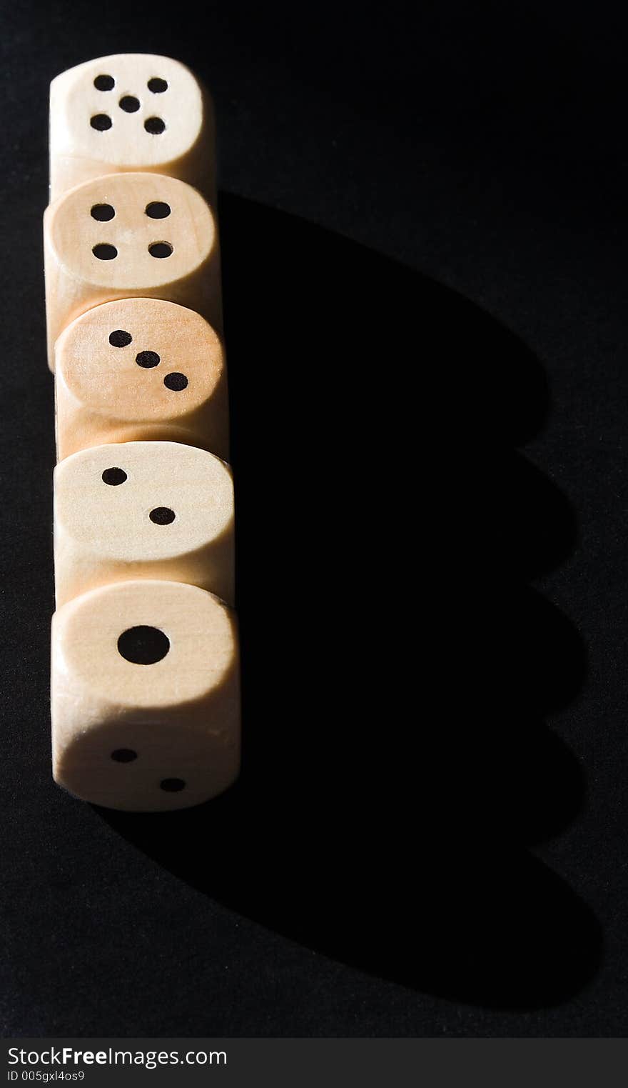 Straight row of wooden dice lit by the sun against a black background.