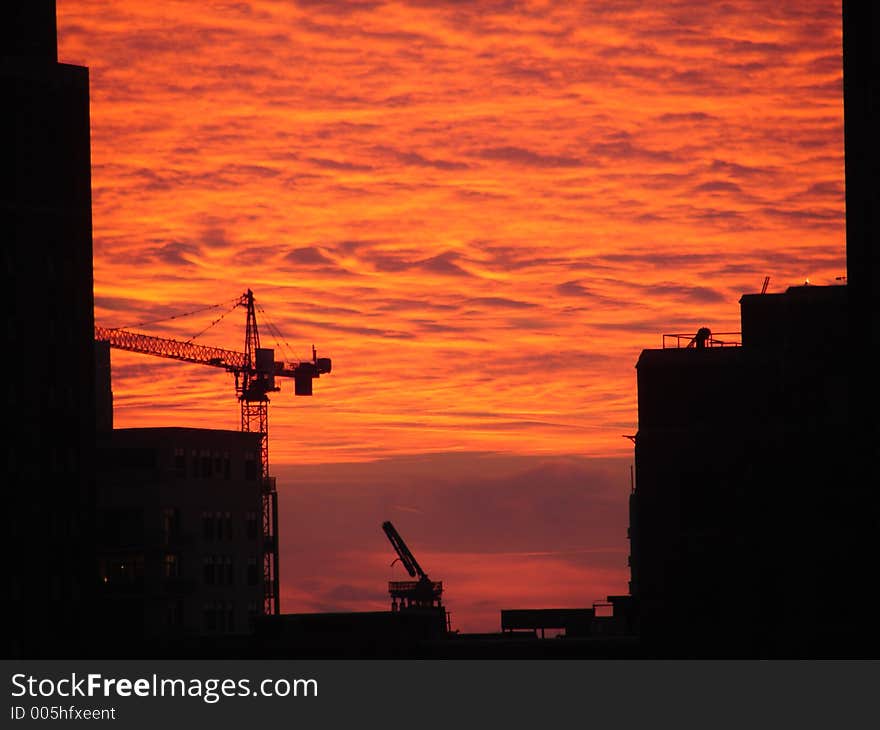 Construction cranes in Chicago building new Apartments silhouetted against a fiery sunset. Construction cranes in Chicago building new Apartments silhouetted against a fiery sunset.