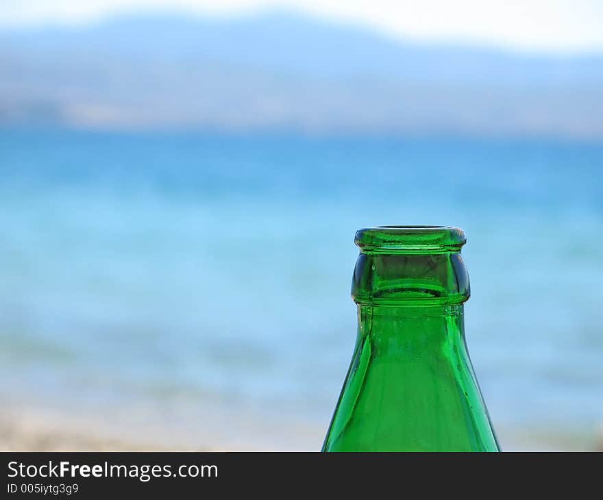 The top of a green beer bottle, against a blue sea background. The top of a green beer bottle, against a blue sea background