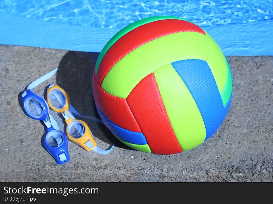 Multicolored ball and glasses by the pool. Multicolored ball and glasses by the pool