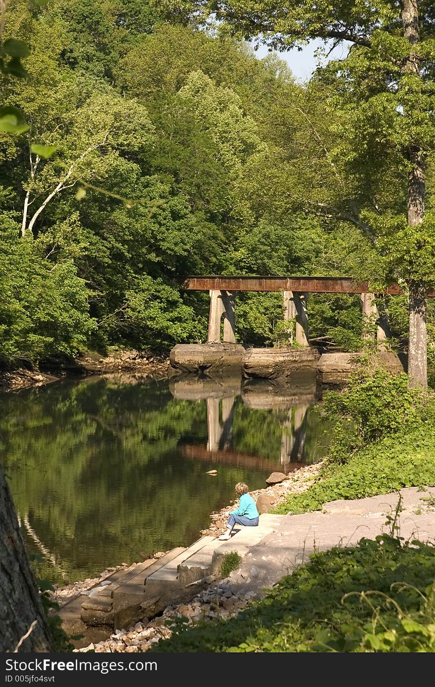 A lady sitting on a riverbank thinking. A lady sitting on a riverbank thinking