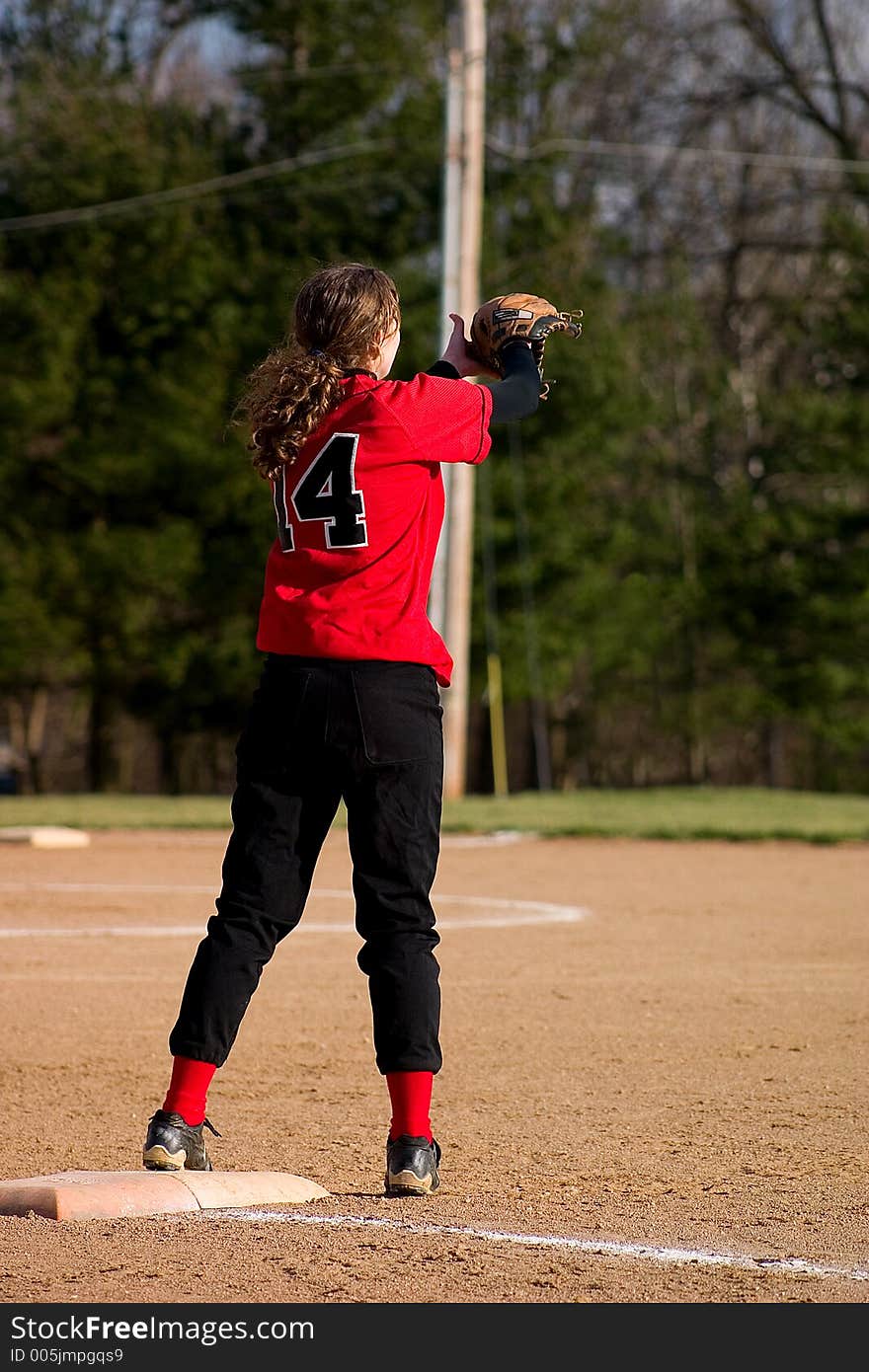 Female softball player. First baseman wearing black pants and a red shirt.