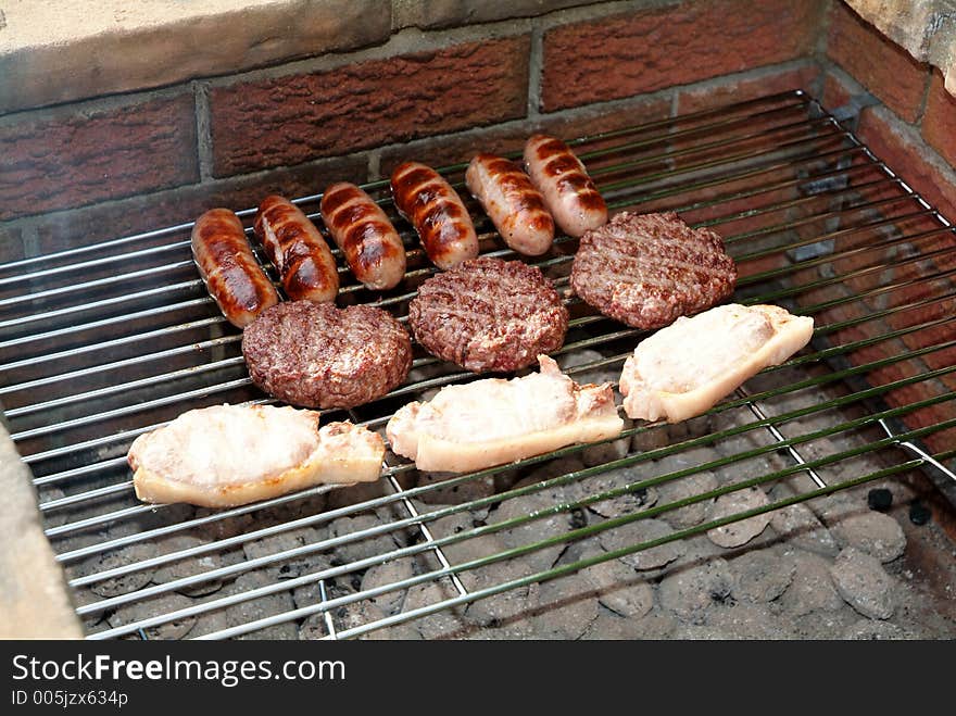 Sausages, burgers, and pork chops cooking on a barbecue. Sausages, burgers, and pork chops cooking on a barbecue.