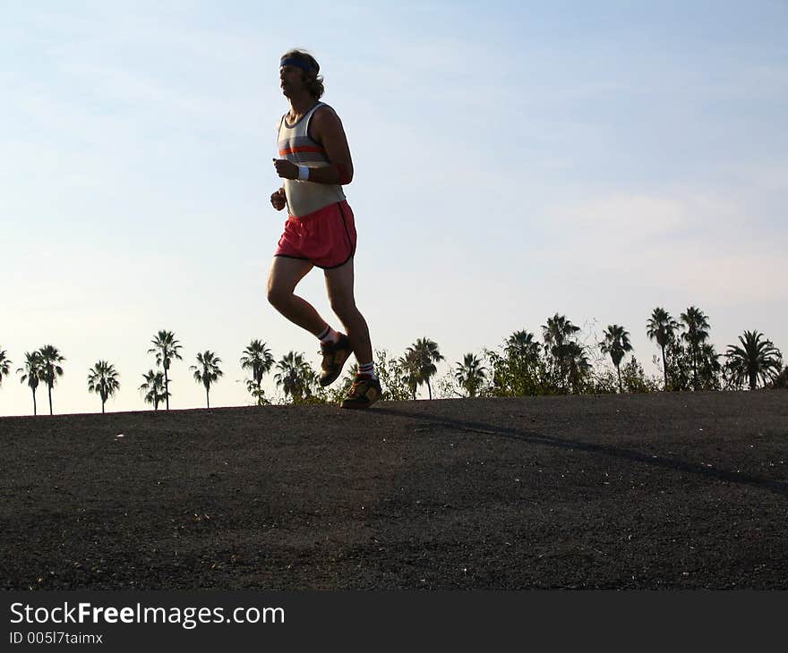 Man running backlit with palm trees in background. Man running backlit with palm trees in background