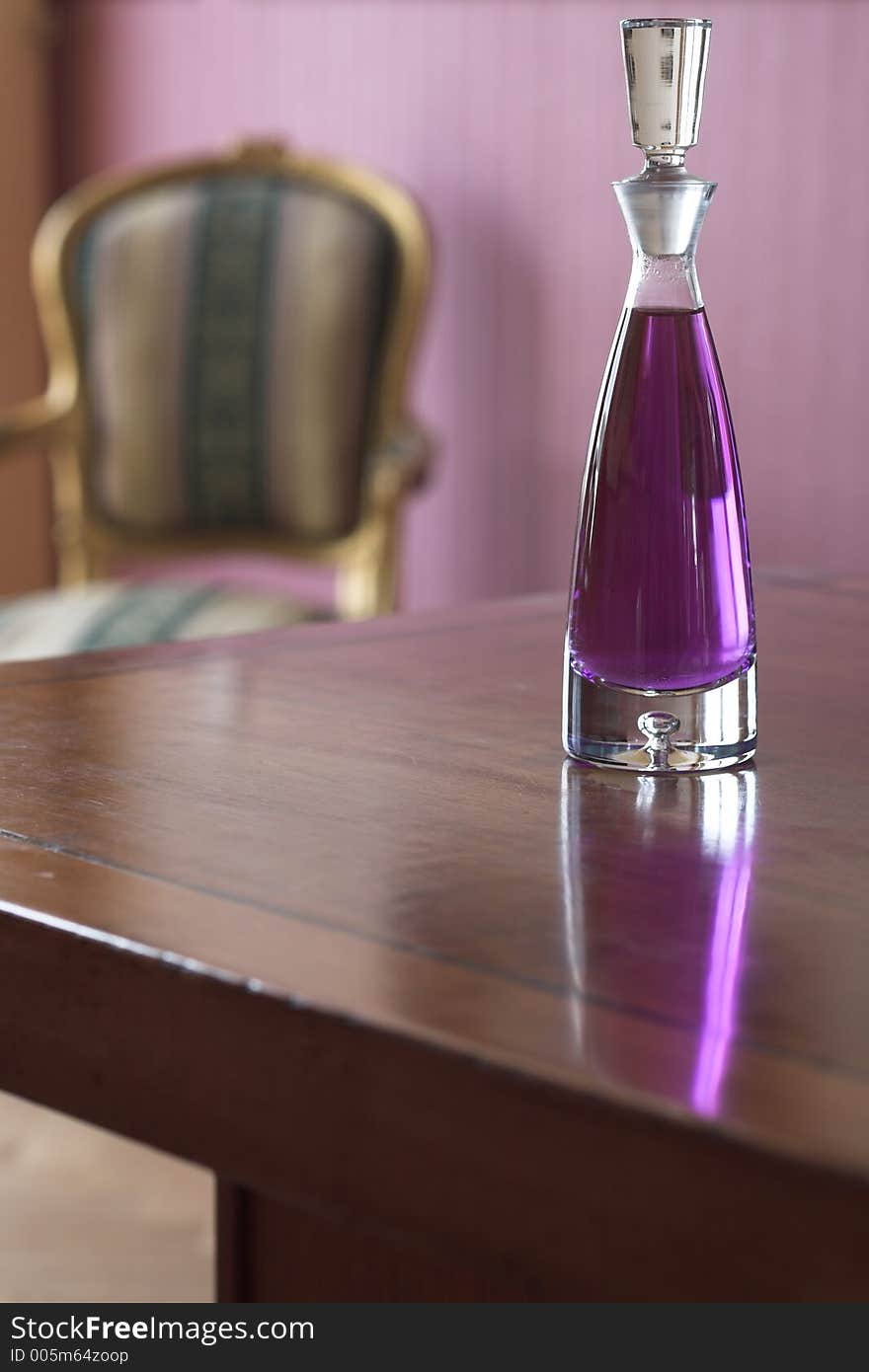 Crystal decanter with purple liquore on top of a wooden table. A classic french chair is seen in the background.