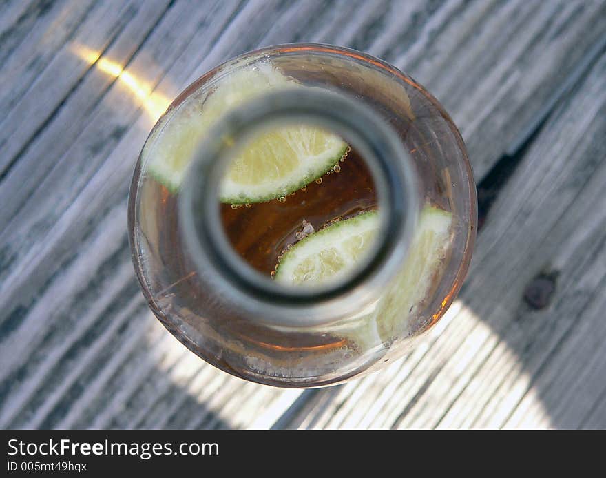 A top-down shot of a beer bottle focusing on delicious limes surrounded by carbonated bubbles on a wooden deck at the beach / ocean. A top-down shot of a beer bottle focusing on delicious limes surrounded by carbonated bubbles on a wooden deck at the beach / ocean.