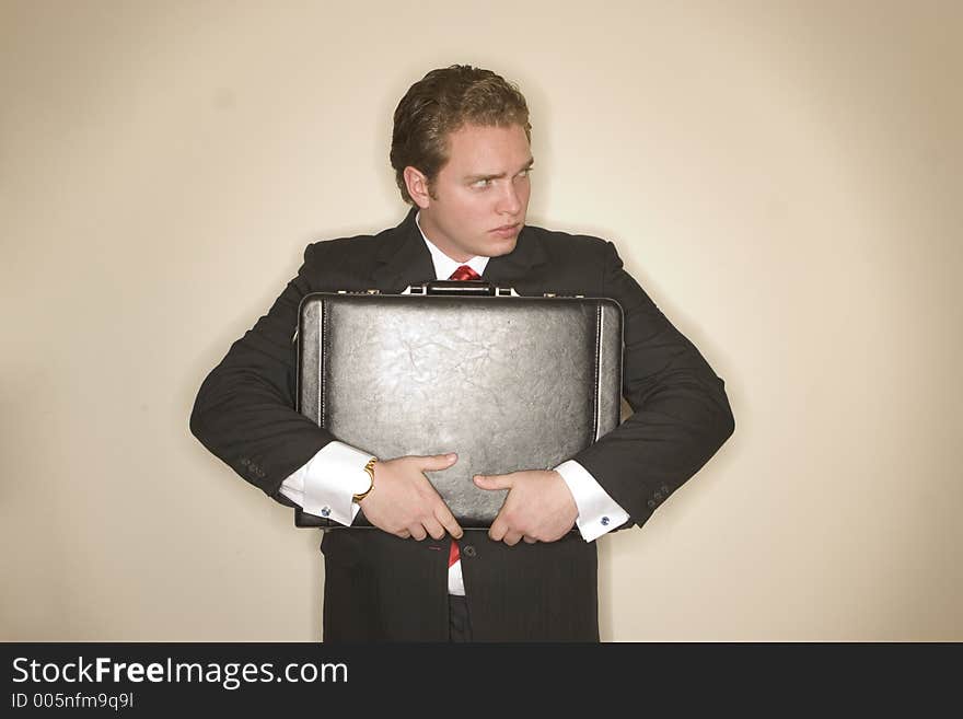 Business man in black suit, red tie, and white shirt is holding briefcase tightly