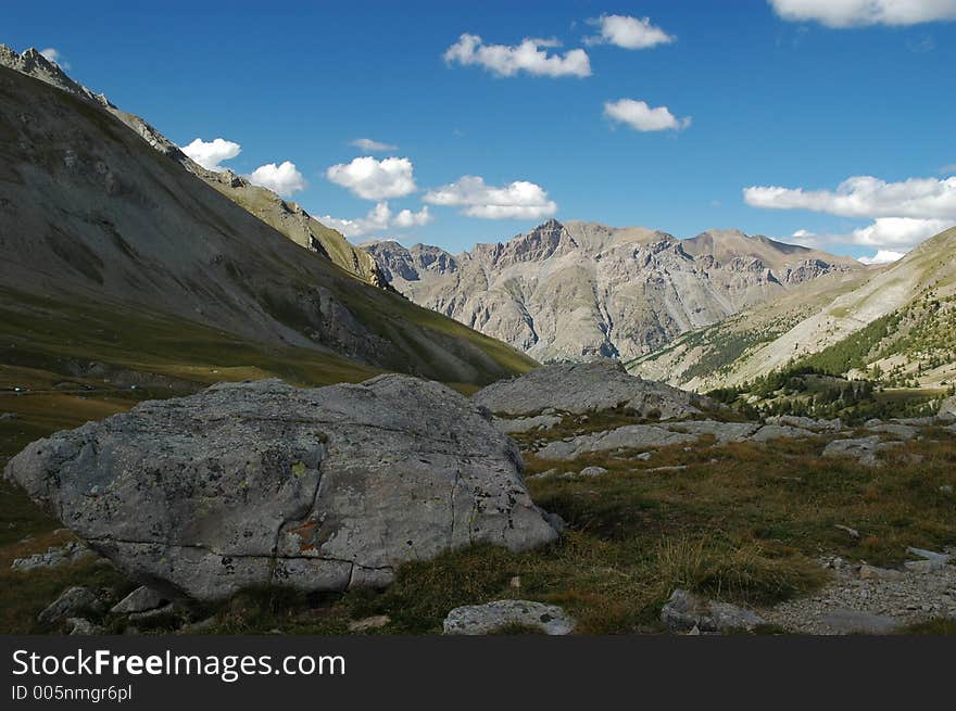 Beautiful mountain scenery against a blue sky seen from the pass. There are boulders in the shade of a mountain. A brightly lit mountain range is in the background. Beautiful mountain scenery against a blue sky seen from the pass. There are boulders in the shade of a mountain. A brightly lit mountain range is in the background.