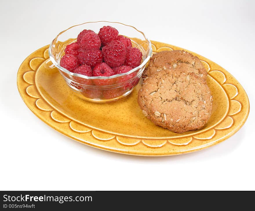 A snack of raspberries and cookies rests on a yellow dish. A snack of raspberries and cookies rests on a yellow dish.