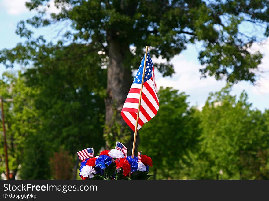 Red, white and blue carnation decoration with American flags in front of a large shade tree. Red, white and blue carnation decoration with American flags in front of a large shade tree