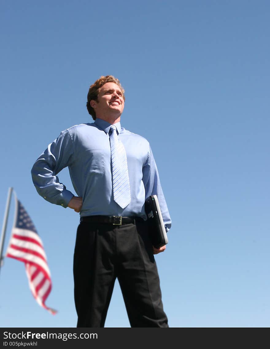 Business man in blue shirt standing in confident pose holding laptop in front of american flag. Business man in blue shirt standing in confident pose holding laptop in front of american flag