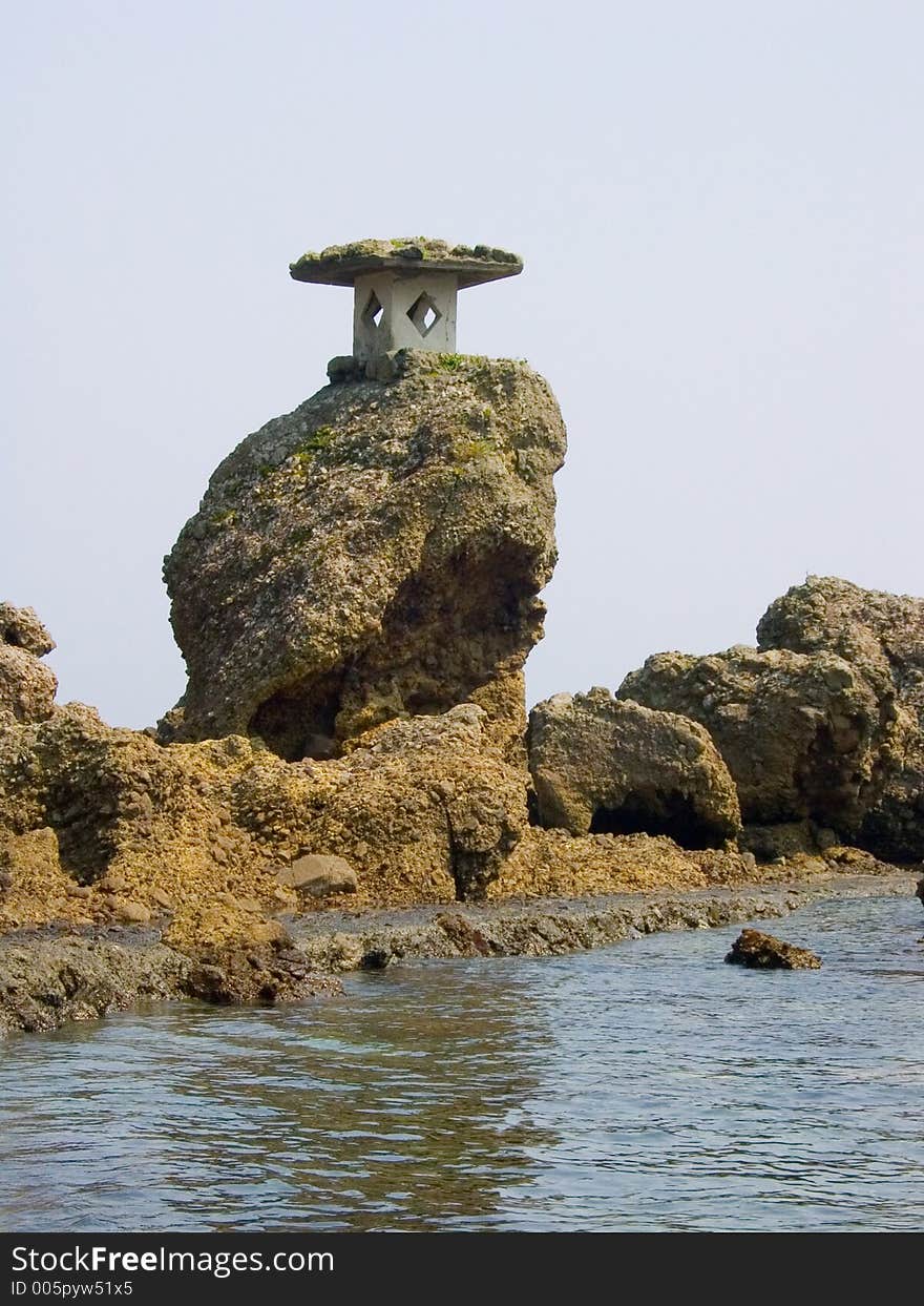 A Japanese stone lantern attached to a rock on the seaside. A Japanese stone lantern attached to a rock on the seaside