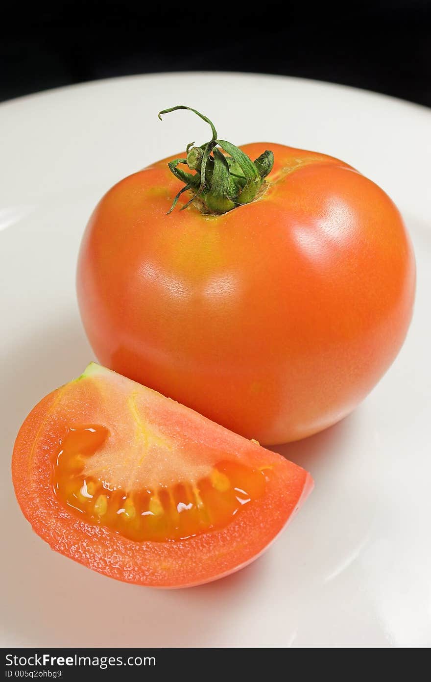 Red tomato and tomato slice on white plate with black background. Red tomato and tomato slice on white plate with black background