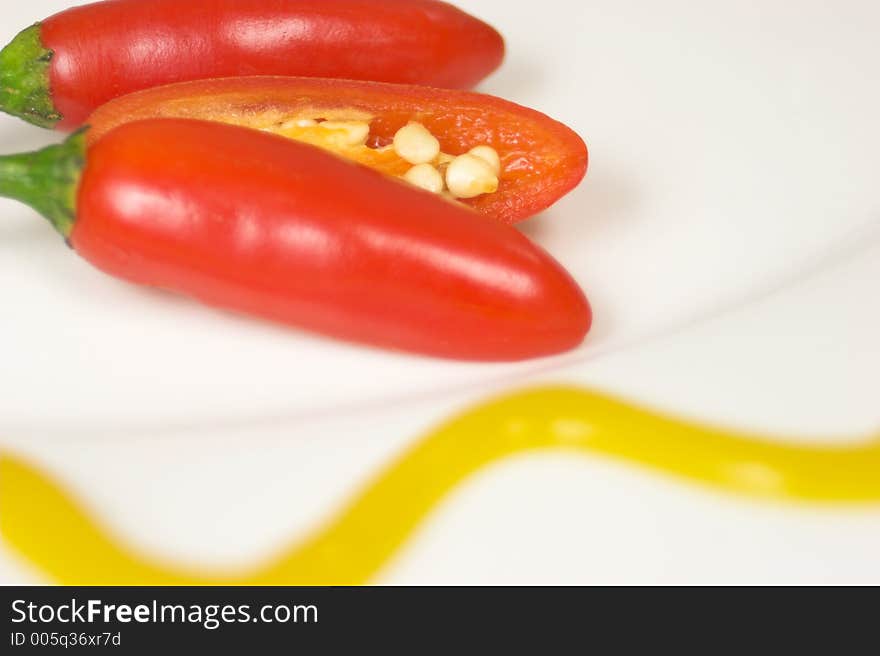 Three chilies on white plate with yellow mustard. Three chilies on white plate with yellow mustard