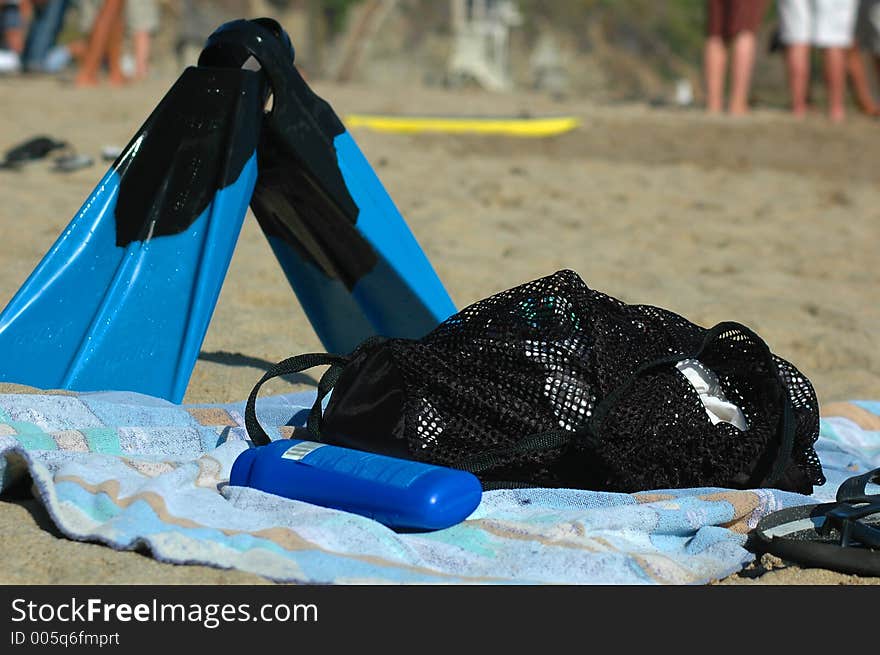 Sunscreen, fins, towel laying on a sandy beach waiting for their use. Sunscreen, fins, towel laying on a sandy beach waiting for their use