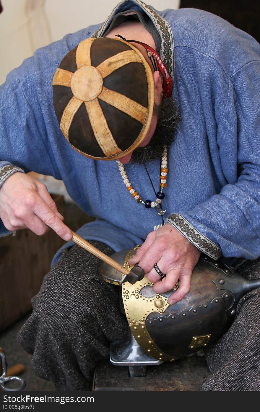 A craftsman chiseling inscription into a medieval soldiers helmet. A craftsman chiseling inscription into a medieval soldiers helmet