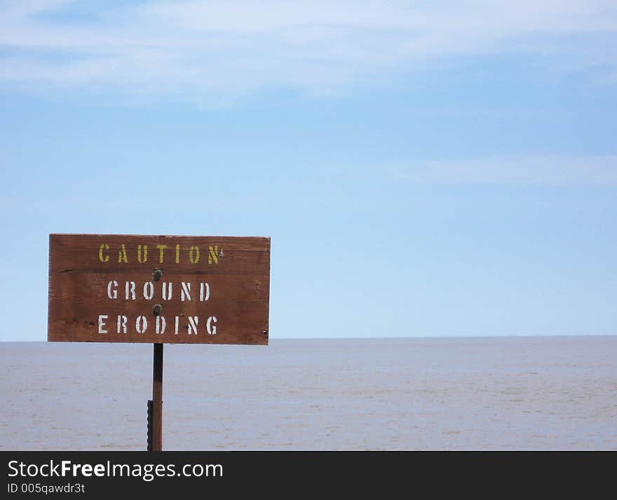 This image depicts a sign near the water's edge stating Caution: Ground Eroding,