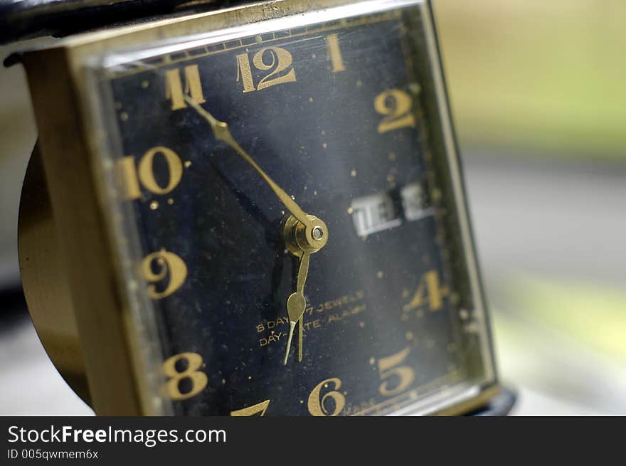 The gold hands and black face of a vintage travel alarm clock. The gold hands and black face of a vintage travel alarm clock