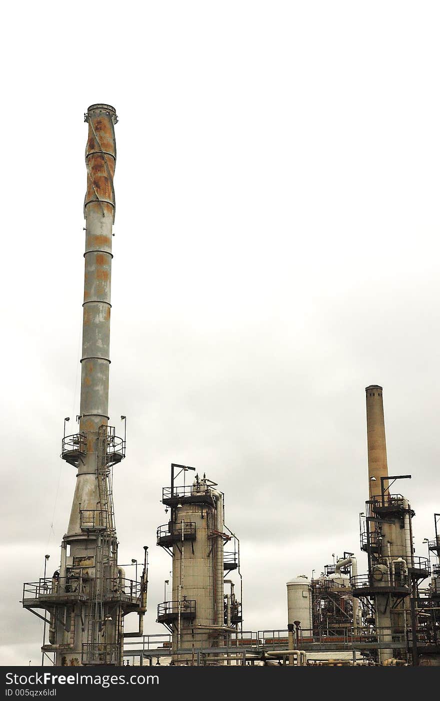 Rusted oil refinery towers against a grey, smoggy background. Rusted oil refinery towers against a grey, smoggy background.