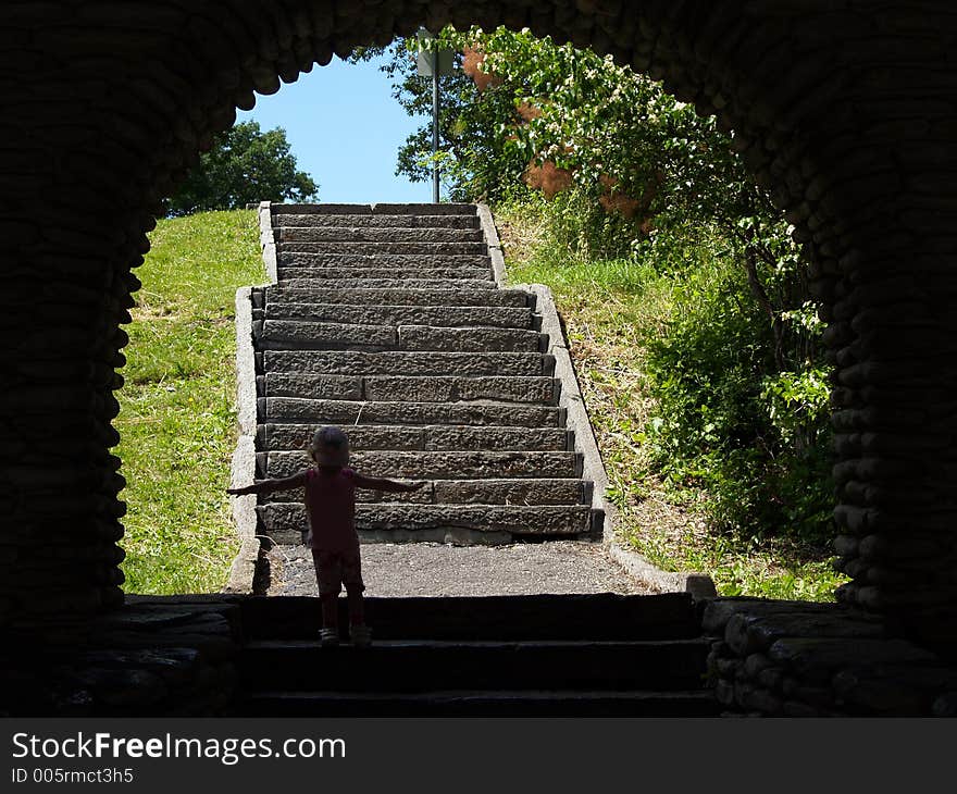 A little girl stands in the shadow of an arch with arms outstretched and stairs in the background. A little girl stands in the shadow of an arch with arms outstretched and stairs in the background.