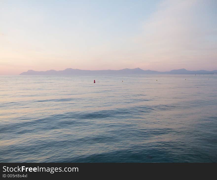 Early morning, calm sea and light red sky over mountains in background. Early morning, calm sea and light red sky over mountains in background