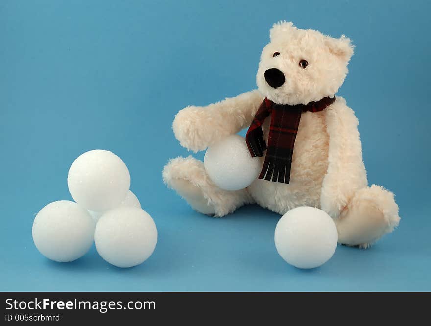 Sitting teddy bear toy with snowballs on blue background. Sitting teddy bear toy with snowballs on blue background