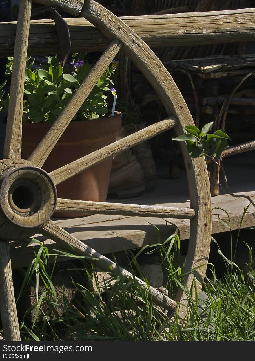 This image was taken of a wagon wheel next to a porch railing with a pot of flowers and chair in the background.