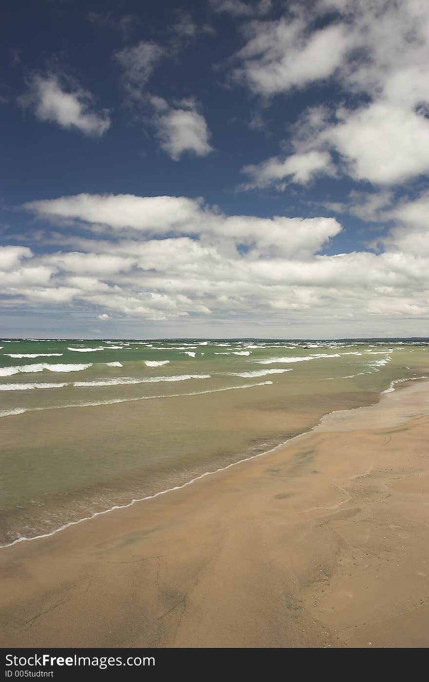 Waves crash along an empty beach on a sunny summer day. Waves crash along an empty beach on a sunny summer day